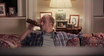 Movie still from “There's Something About Mary” (1998), directed by Bobby Farrelly – A man sitting on a couch drinking a beer; Medium shot, High angle