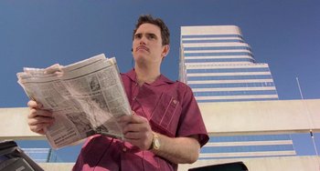 Movie still from “There's Something About Mary” (1998), directed by Bobby Farrelly – A man holding a newspaper while standing in front of a building; Close Up shot, Low angle