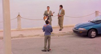 Movie still from “There's Something About Mary” (1998), directed by Bobby Farrelly – Three men in business suits are standing on the side of the road; Wide shot, Over the shoulder angle