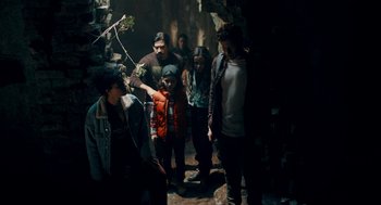 Movie still from “There's Something Wrong with the Children” (2023), directed by Roxanne Benjamin – A group of people standing in a dark room; Medium shot, High angle