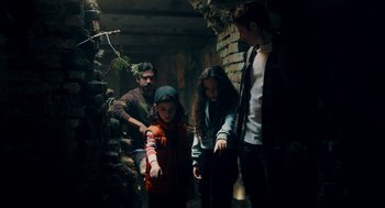 Movie still from “There's Something Wrong with the Children” (2023), directed by Roxanne Benjamin – A group of people standing in a dark room; Medium shot, Low angle