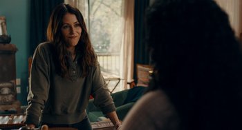 Movie still from “There's Something Wrong with the Children” (2023), directed by Roxanne Benjamin – A woman standing in front of a window in a room; Medium shot, Over the shoulder angle