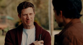 Movie still from “There's Something Wrong with the Children” (2023), directed by Roxanne Benjamin – A man holding a beer in his right hand; Close Up shot, Over the shoulder angle