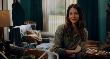 Movie still from “There's Something Wrong with the Children” (2023), directed by Roxanne Benjamin – A woman sitting on a couch in front of a window; Medium shot, Over the shoulder angle