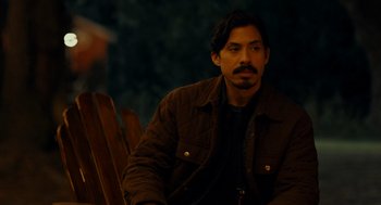 Movie still from “There's Something Wrong with the Children” (2023), directed by Roxanne Benjamin – A man sitting on top of a wooden bench; Medium shot, Over the shoulder angle