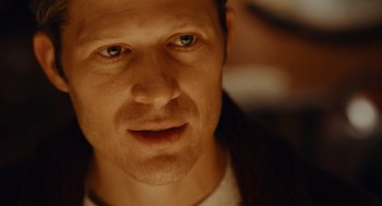 Movie still from “There's Something Wrong with the Children” (2023), directed by Roxanne Benjamin – A man's face in a dimly - lit room; Close Up shot, Over the shoulder angle
