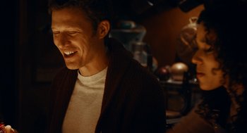 Movie still from “There's Something Wrong with the Children” (2023), directed by Roxanne Benjamin – A man smiling while standing in front of a camera; Close Up shot, Over the shoulder angle