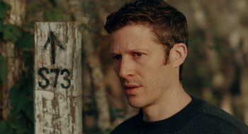 Movie still from “There's Something Wrong with the Children” (2023), directed by Roxanne Benjamin – A person wearing a black t - shirt; Close Up shot, Over the shoulder angle