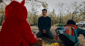 Movie still from “There's Something Wrong with the Children” (2023), directed by Roxanne Benjamin – A man sitting on the ground in front of a group of people; Medium shot, Over the shoulder angle