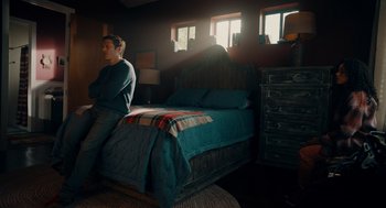 Movie still from “There's Something Wrong with the Children” (2023), directed by Roxanne Benjamin – A man sitting on the edge of a bed in a bedroom; Wide shot, High angle