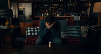 Movie still from “There's Something Wrong with the Children” (2023), directed by Roxanne Benjamin – A man sitting on a couch with his hands over his face; Medium shot, High angle