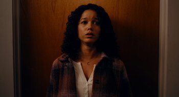 Movie still from “There's Something Wrong with the Children” (2023), directed by Roxanne Benjamin – A woman with curly black hair wearing a white shirt and a plaid jacket; Medium shot, High angle