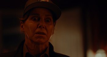 Movie still from “There's Something Wrong with the Children” (2023), directed by Roxanne Benjamin – An older woman wearing a hat and looking surprised; Close Up shot, Over the shoulder angle