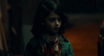 Movie still from “There's Something Wrong with the Children” (2023), directed by Roxanne Benjamin – A young girl is standing in a dark room; Close Up shot, Over the shoulder angle