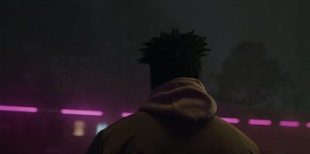 Movie still from “They Cloned Tyrone” (2023), directed by Juel Taylor – A man with a hoodie on looking into the night sky; Close Up shot, Over the shoulder angle