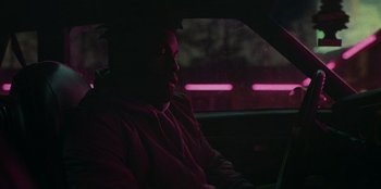 Movie still from “They Cloned Tyrone” (2023), directed by Juel Taylor – A man sitting in the back of a car at night; Medium shot, Over the shoulder angle