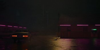 Movie still from “They Cloned Tyrone” (2023), directed by Juel Taylor – A car parked on the side of the road at night; Extreme Wide shot, Low angle