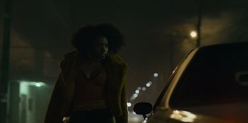 Movie still from “They Cloned Tyrone” (2023), directed by Juel Taylor – A woman standing next to a car on a street; Medium shot, Low angle