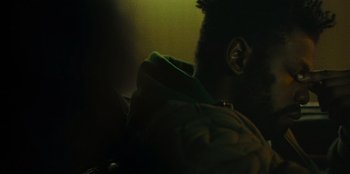 Movie still from “They Cloned Tyrone” (2023), directed by Juel Taylor – A person with a green jacket is looking out the window at night; Extreme Close Up shot, Over the shoulder angle
