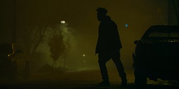 Movie still from “They Cloned Tyrone” (2023), directed by Juel Taylor – A man walking on a street at night with trees in the background; Wide shot, Low angle