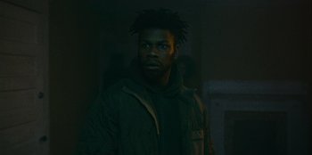 Movie still from “They Cloned Tyrone” (2023), directed by Juel Taylor – A man with a dreadlocks standing in a dark room; Close Up shot, Low angle