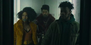 Movie still from “They Cloned Tyrone” (2023), directed by Juel Taylor – A group of people standing next to each other in a room; Medium shot, Low angle