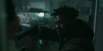 Movie still from “They Cloned Tyrone” (2023), directed by Juel Taylor – A man holding a gun in a dark room; Close Up shot, Low angle