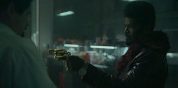 Movie still from “They Cloned Tyrone” (2023), directed by Juel Taylor – A man holding a gun while standing next to a window; Medium shot, Low angle