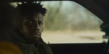 Movie still from “They Cloned Tyrone” (2023), directed by Juel Taylor – A person in a car looking at the camera; Close Up shot, Over the shoulder angle