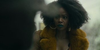 Movie still from “They Cloned Tyrone” (2023), directed by Juel Taylor – A black woman with blue lipstick looking at the camera through a window; Close Up shot, Over the shoulder angle
