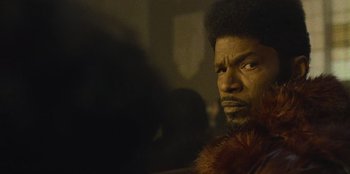 Movie still from “They Cloned Tyrone” (2023), directed by Juel Taylor – A person wearing a fur coat; Close Up shot, Over the shoulder angle