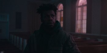 Movie still from “They Cloned Tyrone” (2023), directed by Juel Taylor – A man with dreadlocks standing in a dark room; Close Up shot, Low angle