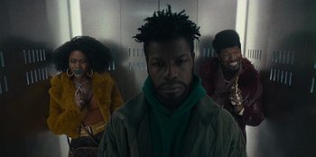Movie still from “They Cloned Tyrone” (2023), directed by Juel Taylor – A man in a green jacket and two other people in a elevator; Medium shot, Low angle