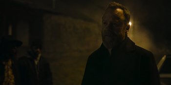 Movie still from “They Cloned Tyrone” (2023), directed by Juel Taylor – A man with a beard is standing in the dark; Close Up shot, Over the shoulder angle