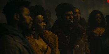 Movie still from “They Cloned Tyrone” (2023), directed by Juel Taylor – A group of people standing in a room; Medium shot, Low angle