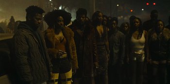 Movie still from “They Cloned Tyrone” (2023), directed by Juel Taylor – A group of people standing in the dark; Medium shot, High angle