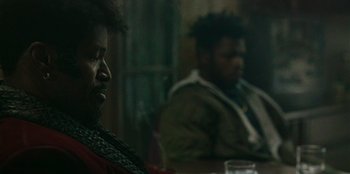 Movie still from “They Cloned Tyrone” (2023), directed by Juel Taylor – Two people sitting at a table in a dark room; Close Up shot, Over the shoulder angle