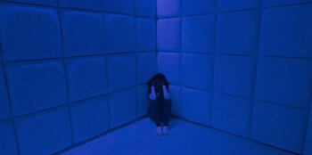 Movie still from “They Cloned Tyrone” (2023), directed by Juel Taylor – A cat sitting in a corner of a room with blue lighting; Wide shot, High angle