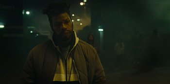 Movie still from “They Cloned Tyrone” (2023), directed by Juel Taylor – A man in a jacket standing in the dark; Medium shot, Low angle