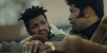 Movie still from “They Cloned Tyrone” (2023), directed by Juel Taylor – A man with dreadlocks is looking at another man with dreadlocks; Close Up shot, Over the shoulder angle