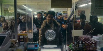 Movie still from “They Cloned Tyrone” (2023), directed by Juel Taylor – A group of men standing around a table with drinks on it; Medium shot, Over the shoulder angle