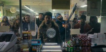 Movie still from “They Cloned Tyrone” (2023), directed by Juel Taylor – A group of people standing around a store; Medium shot, Over the shoulder angle