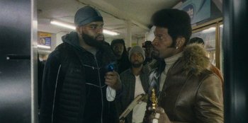 Movie still from “They Cloned Tyrone” (2023), directed by Juel Taylor – Two men are talking to each other in a crowd of people; Medium shot, Over the shoulder angle