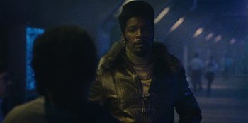 Movie still from “They Cloned Tyrone” (2023), directed by Juel Taylor – A man in a leather jacket and a fur collar; Close Up shot, Low angle