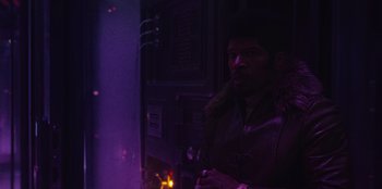 Movie still from “They Cloned Tyrone” (2023), directed by Juel Taylor – A man standing next to a fire in a dark room; Medium shot, Over the shoulder angle