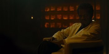 Movie still from “They Cloned Tyrone” (2023), directed by Juel Taylor – A man sitting on a chair in a room; Medium shot, Low angle