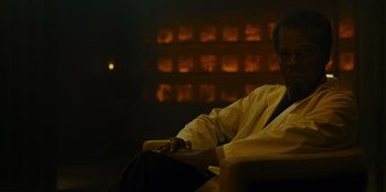 Movie still from “They Cloned Tyrone” (2023), directed by Juel Taylor – A man sitting on a chair in a room; Medium shot, Low angle