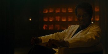 Movie still from “They Cloned Tyrone” (2023), directed by Juel Taylor – A man sitting on a couch in a room; Close Up shot, Over the shoulder angle