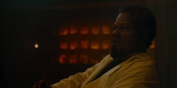 Movie still from “They Cloned Tyrone” (2023), directed by Juel Taylor – A man sitting in front of a fire place; Close Up shot, Over the shoulder angle
