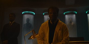Movie still from “They Cloned Tyrone” (2023), directed by Juel Taylor – A man in a lab coat standing in front of a lamp; Medium shot, Low angle